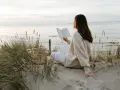 Kobieta czyta książkę na plaży, ciesząc się spokojem i świeżym powietrzem. To idealny moment, by poczuć, kiedy jest najwięcej jodu nad morzem.