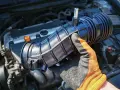 Hand in glove holds a new p0172 chevy air intake hose, ready to be installed on the engine.