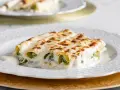 Cannelloni ricotta e spinaci fumanti, ricoperti da besciamella e formaggio fuso, serviti su un piatto bianco.