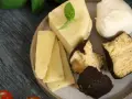 Różnorodne rodzaje serów na talerzu: kawałki żółtego sera, kulka mozzarelli i ser w ciemnej skórce.