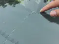 Palec wskazujący na pękniętej szybie samochodowej. Sprawdź autoglass cennik, aby poznać koszt naprawy.