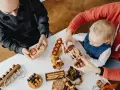 Rodzina bawi się drewnianymi łamigłówkami. Dziecko z rodzicami rozwiązuje zagadki, przygotowując się do przedszkola.