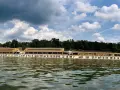 Das Strandbad Wannsee mit seiner langen Promenade und vielen Liegestühlen, im Hintergrund grüne Bäume und ein bewölkter Himmel.