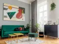 Soggiorno moderno con divano verde smeraldo e tavolini dorati. L'arte astratta sul muro grigio e i mobili scuri creano un perfetto abbinamento colori pareti e mobili.
