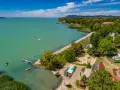 Słoneczny dzień na kempingu Balaton. Ludzie kąpią się w jeziorze i basenie, bawią na placu zabaw, a kampery stoją wśród drzew.