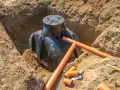 Instalacja szamba w wykopie, przygotowanie do zasypania. Widać rury drenażowe i akcesoria, kluczowe dla prawidłowego montażu i pytania jak głęboko zakopać rury drenażowe.