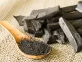 Morceaux de charbon actif et poudre dans une cuillère en bois. On se demande en combien de temps agit le charbon actif pour une détox.