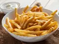 Chrupiące frytki z airfryer w białej misce, obok sos. Idealna przekąska na każdy dzień.