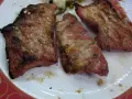 Tres trozos de secreto de cerdo a la parrilla, jugosos y con sal gruesa, servidos en un plato blanco con borde rojo.