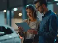 Kobieta i mężczyzna patrzą na tablet, stojąc obok samochodu.