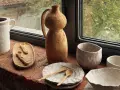 Ceramica fatta in casa: vasi, ciotole e cucchiaini grezzi, posati su un davanzale di mattoni, con vista su un giardino verde.