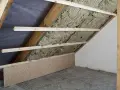 Izolacja wełną mineralną na poddaszu, widoczne drewniane belki konstrukcyjne i płyta OSB.