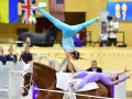 Deux gymnastes réalisent une performance de gymnastique cheval. L'une est en équilibre sur les mains, l'autre allongée sur le dos du cheval.