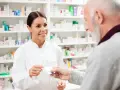 Uśmiechnięta farmaceutka podaje starszemu panu leki. W tle apteczne półki pełne leków, w tym poltixa.