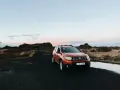 Pomarańczowy samochód na czarnej, wulkanicznej drodze. Islandia oferuje malownicze krajobrazy i swobodny ruch drogowy.