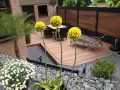 Giardino moderno senza erba: deck in legno, ghiaia, piante in vaso e fiori bianchi. Esempi idee giardino senza erba.