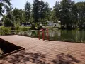 Drewniany pomost z czerwonymi poręczami nad jeziorem. W tle drzewa, budynki i samochody. Idealne miejsce na łagów camping.