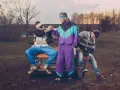 Trzech mężczyzn w dresach i swetrach, symbolizujących modę lat 90. w Polsce, siedzi na starym samochodzie.