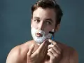 Hombre con espuma de afeitar en la cara, aprendiendo como afeitarse la barba con una maquinilla.