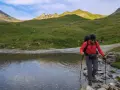 Un randonneur traverse un ruisseau de montagne, bâtons en main. Une belle illustration de pourquoi marcher avec des bâtons pour plus de stabilité.
