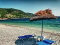 Plaża z leżakami i parasolem, w tle zielone wzgórza i turkusowe morze. To idealne miejsce na wypoczynek na grupie wysp na Morzu Egejskim.