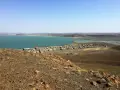Widok na osadę nad turkusowym jeziorem Turkana. W oddali widać górzysty krajobraz.
