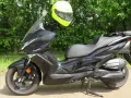 Czarny skuter Kawasaki J300 z jaskrawożółtym kaskiem zawieszonym na kierownicy, gotowy do jazdy w słoneczny dzień.
