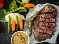 Succulenta costata di manzo affettata, servita con purè, verdure miste e salsa al pepe verde.