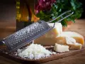 Tarka z grudkami startego parmezanu i kawałkami sera na desce. Obok butelka oliwy i zielenina.