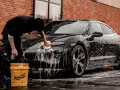 Person tvättar en svart bil med Autoglym-produkter. Två gula hinkar står bredvid.