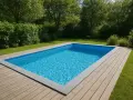En inbjudande pool med klart blått vatten, omgiven av en träaltan och grönskande träd. Cellplast under poolen ger stabilitet och isolering.