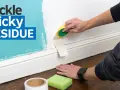 Learn how to get adhesive off wall with this guide. A hand uses a sponge to remove tape residue from a painted wall.