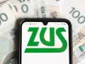 Telefon z logo ZUS na tle polskich banknotów 100 zł.