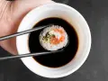 Pałeczkami zanurzam sushi w sosie do sajgonek. Widać kawałek łososia i ryż.