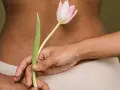 Delikatne rozstępy na plecach, ukryte za tulipanem. Ciało w beżowej bieliźnie.