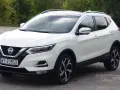 Biały Nissan Qashqai 2014 z polskimi tablicami rejestracyjnymi stoi na drodze, otoczony zielenią drzew.