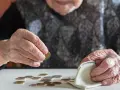 Dłoń starszej osoby liczy monety, zastanawiając się, kiedy najlepiej przejść na emeryturę w 2026 roku.