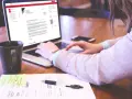 Kobieta pisze list motywacyjny sprzedawca na laptopie, obok kubek kawy i notatki.