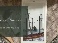 Karta Tarota "Sześć Mieczy" przedstawia łódź z sześcioma mieczami, symbolizującą podróż i przejście.