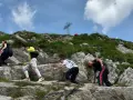Grupa turystów wspina się po kamienistym zboczu, pokonując najtrudniejszy szlak na Giewont. W tle widoczny krzyż.