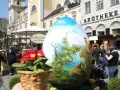 Großes, bemaltes Ei mit Frühlingslandschaft und Hahn, ein Osterbrunnen, der erklärt, warum ist Ostern immer wann anders.