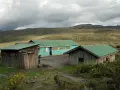 Proste chatki z zielonymi dachami na tle surowego krajobrazu u podnóża góry Mt Kenya.