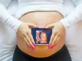 Ręce z różowymi paznokciami obejmują brzuch, na którym widnieje zdjęcie z 8 tygodnia ciąży usg 3d.