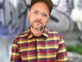 Filip Springer w okularach i koszuli w kratę, na tle graffiti.