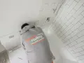A person in a "Correct Caulking" hoodie works on a bathtub, demonstrating how to caulk a bathtub with white subway tiles in the background.