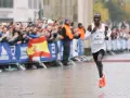 Eliud Kipchoge corre in una maratona, mostrando quanto è lunga una maratona. Pubblico festante e bandiera spagnola sullo sfondo.