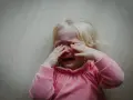 Małe dziecko płacze, zasłaniając oczy rękami. Wygląda, jakby dziecko uderzało głową o ścianę z frustracji.