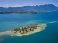 L'isola dei conigli sul Lago di Garda, un gioiello verde con case e alberi, circondata da acque turchesi e montagne sullo sfondo.