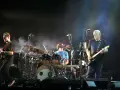 Les membres de Pink Floyd sur scène, David Gilmour à la guitare, Nick Mason à la batterie, et un autre musicien.