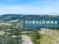 Widok na Gubałówkę z panoramą Tatr. Widać zabudowania, lasy i góry w oddali.